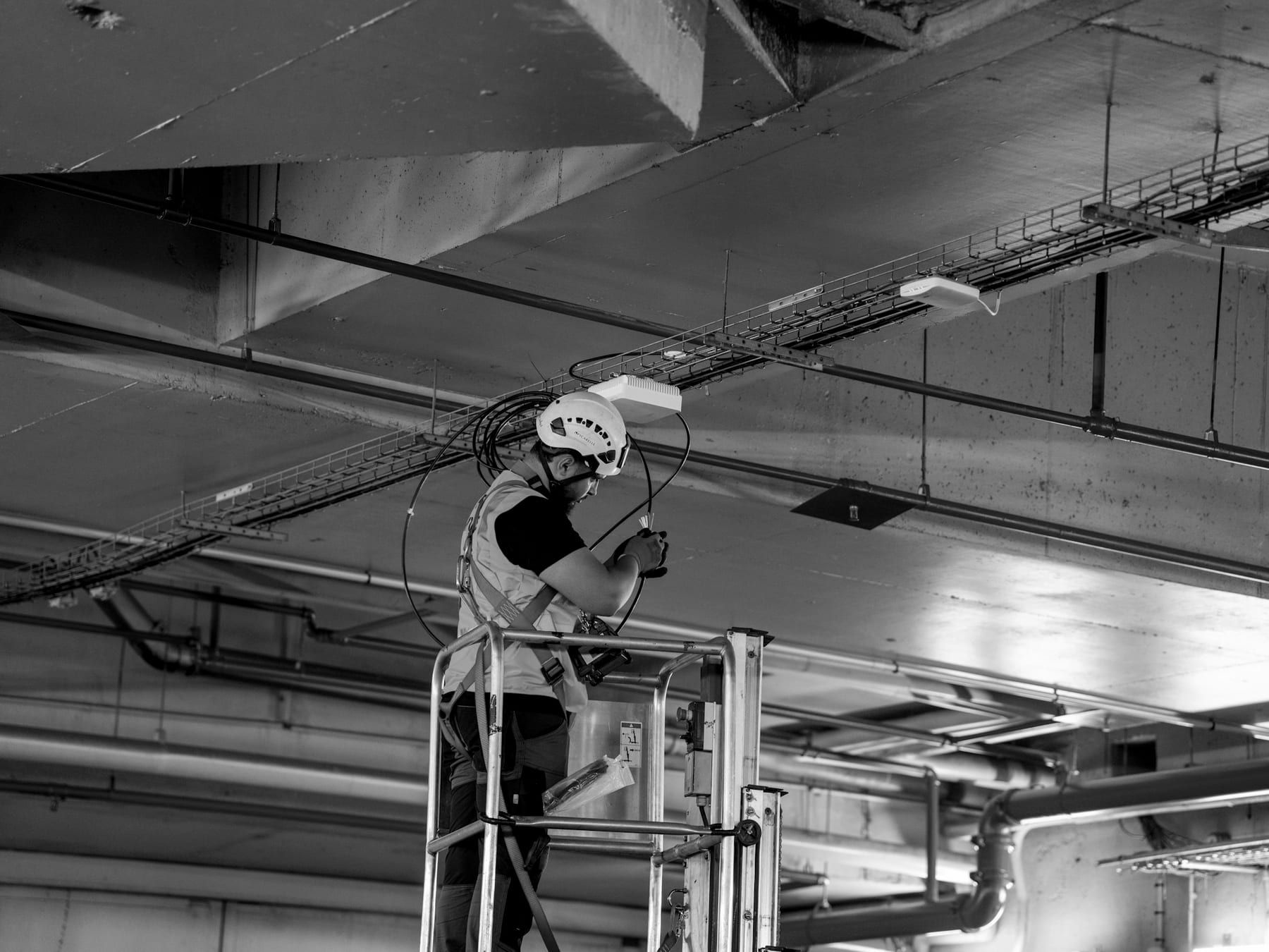 MEP technician on a lift installing cables along ceiling services